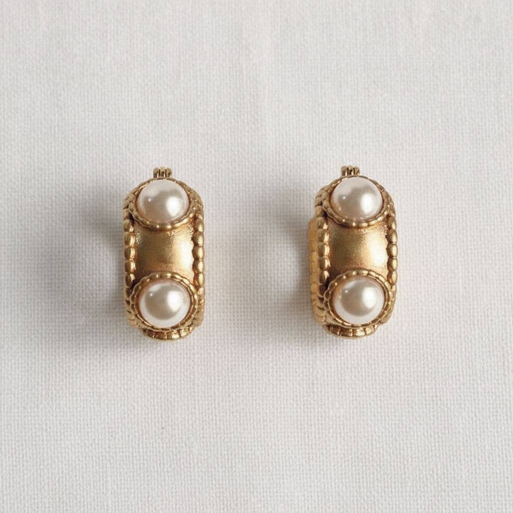 Pair of gold earrings with pearl-like stones on a light gray background