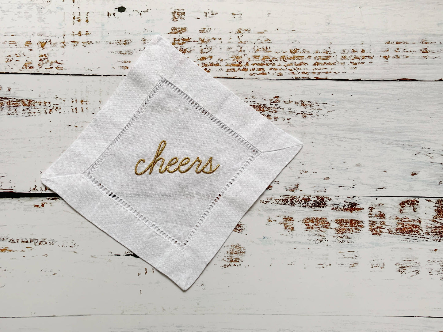White napkin with 'cheers' embroidery on a rustic wooden surface