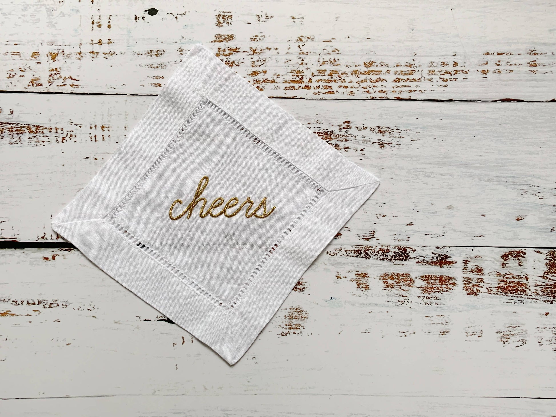 White napkin with 'cheers' embroidery on a rustic wooden surface